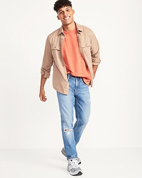 A model wears Skinny style denim with a tan button-up shirt over a peach colored t-shirt