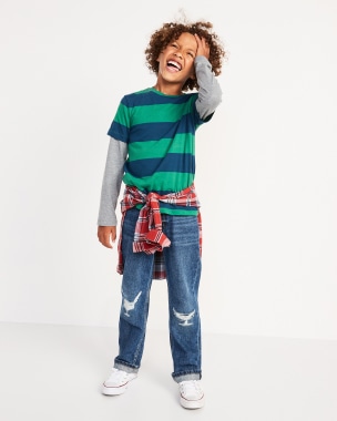 A young model holding his hair and wearing a striped green t-shirt and loose jeans.