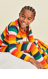 A young model is wearing stripped rainbow color pajamas.