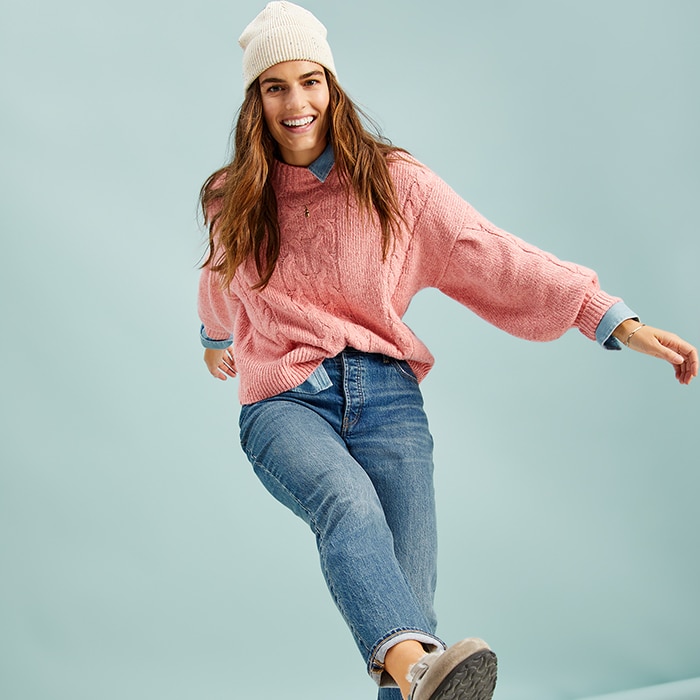 A female model wears pink mock-neck heathered cable-knit sweater and jeans