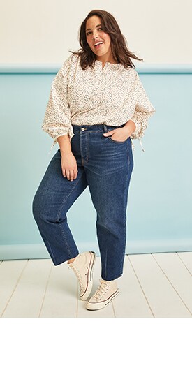 A female model wears dark-washed jeans and light colored floral print top
