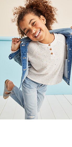 A female model wearing white half button tops, light washed jeans and a jean jacket.