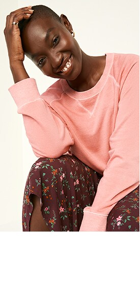 Une femme porte une longue jupe fleurie et un chandail en coton ouaté ras du cou rétro rose pâle spécialement teint.