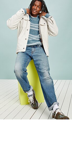 Un homme porte un jean semi-évasé à Extensibilité intégrée au fini moyen, une veste épaisse de couleur pâle et un chandail rayé.