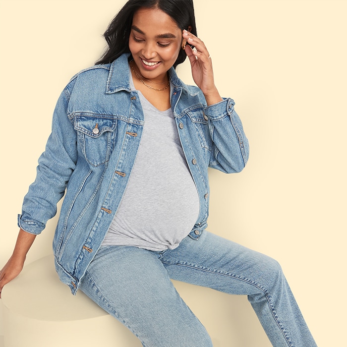 A maternity model wears a denim jacket, heather grey v-neck tee shirt and light-wash jeans.