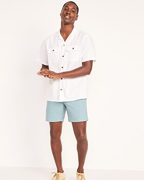 Un homme porte une chemise à manches courtes blanche et un short kaki rodé bleu pâle.
