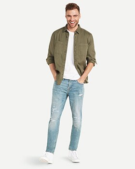 A male model wears Relaxed Slim Taper style denim and a green button up shirt over a white t-shirt.
