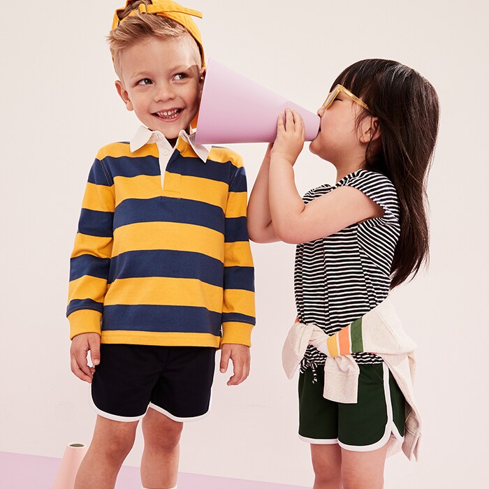 A young boy model wearing striped long sleeve rugby polo shirt and girl model dressed in stripe top.