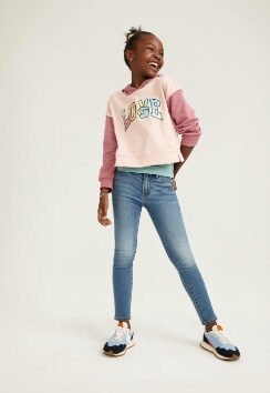 A female model wears Super-Skinny style jeans with a pink layered crew neck sweatshirt.