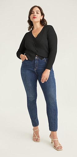 A model in dark wash skinny jeans with mid-rise and a black blouse.