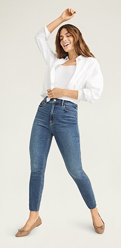 A female model in medium wash high waisted ankle cut skinny jeans paired with a white top.