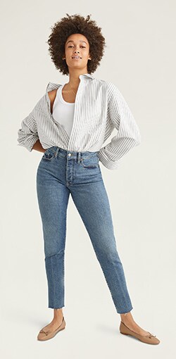 A model in a pinstripe button down with a white tank tucked into distessed curvy fit jeans.