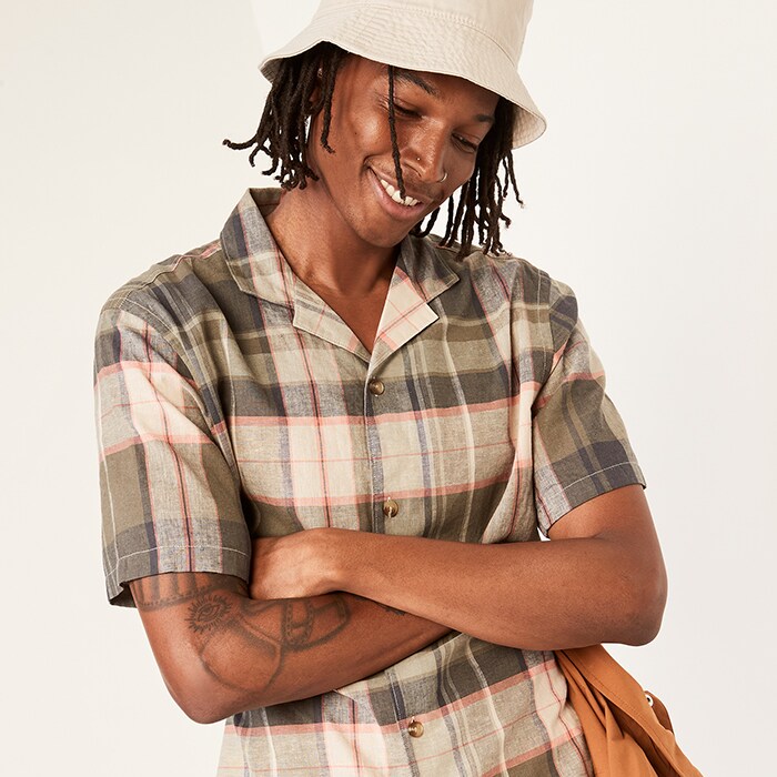 A male model wears a brown & beige plaid button-up short-sleeve shirt & bucket hat.