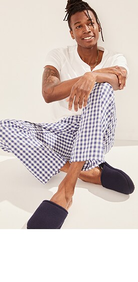 A male model wears a white pajama t-shirt & check patterned pajama pants.