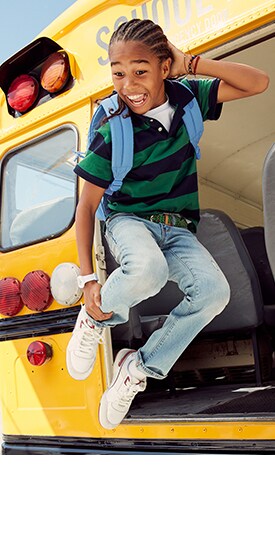 Un jeune garçon sautant d’un autobus scolaire porte un polo à rayures de rugby et un jean.