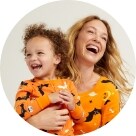 A female model holding a toddler both wearing matching Halloween pajamas.