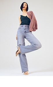 A woman in a dark v-neck tank top, a cardigan draped over her shoulder, and high-waisted wide leg jeans with a pair of kitten heels.