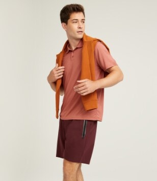 A male model wears a light red polo shirt and dark red activewear shorts.
