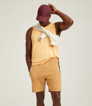 A male model wears a yellow tank top & light yellow activewear shorts.