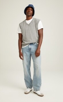 A male model wears Loose style jeans & a grey v-neck sweater vest