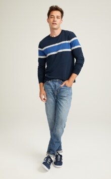 A male model wears Relaxed Slim Taper style denim & a striped crew neck sweater.