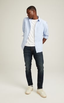 A male model wears Skinny style denim with a light blue button up shirt