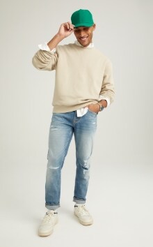 A male model wears light washed Slim style jeans & a cream colored sweater.