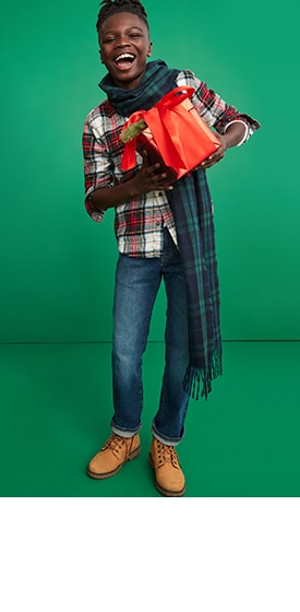 A young model wearing slim fit Old Navy jeans for boys with plaid shirt, scarf and lace-up boots.