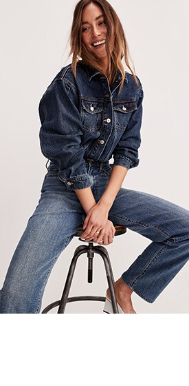 A female model wears a dark denim jacket and dark wash jeans.