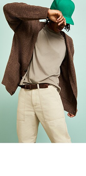 A male model wears a dark cardigan over a cream t-shirt and light khakis.