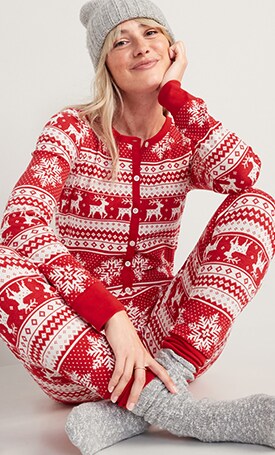 A female model wears red  holiday print pajamas with grey beanie and socks.