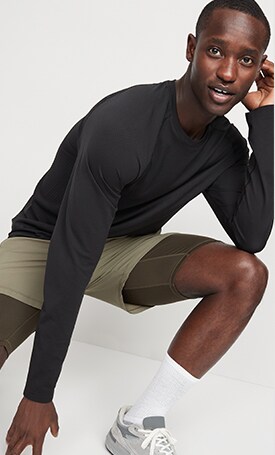 A male model wears a black long sleeve active T-shirt and green shorts.