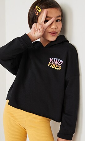 A girl dressed in a black graphic print hoodie paired with yellow leggings and yellow hairclips.