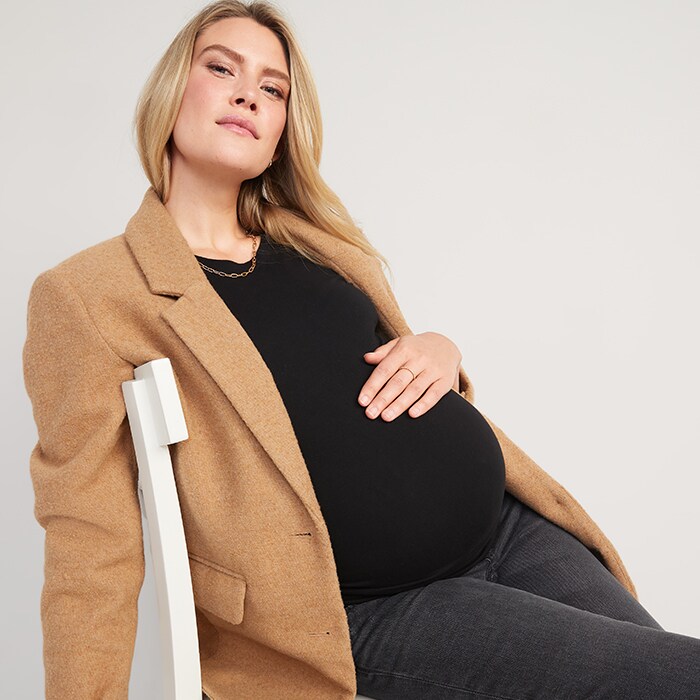 A maternity model wears a light brown coat and black maternity top