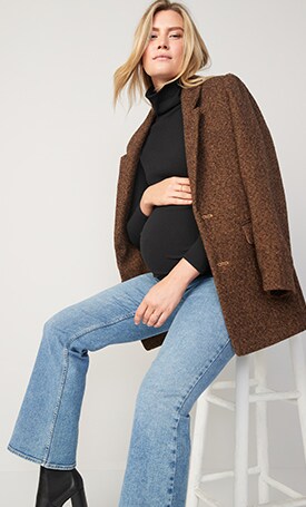 A female model wears light washed maternity jeans & a brown coat