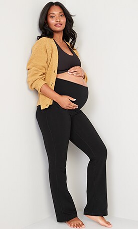 A maternity model wears black flared leggings & a yellow sweater