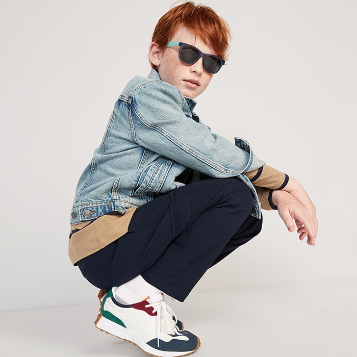 A young model wearing  dark pants, a striped longsleeve shirt, denim jean jacket, and sneakers.