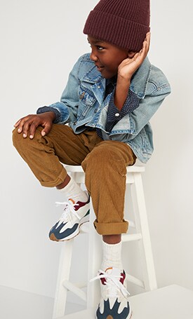 A young boy dressed in khaki pants, denim jacket, and a beanie.