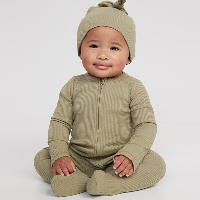 A baby model wearing green footed one-piece and matching hat.