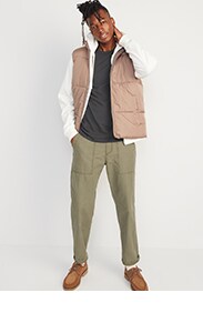 A male model wears olive green pants with a navy blue shirt and tan vest.