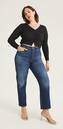 A model in a cropped black cardigan with high waisted curvy straight jeans.