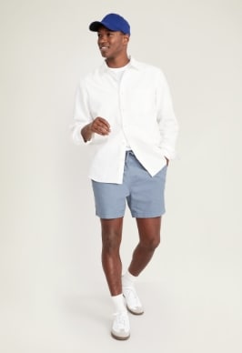 A male model wears a pair of light blue jogger style shorts & a white long sleeve button up shirt.