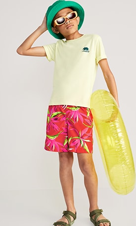 A male model dressed in floral patterned Printed Swim Trunks & light yellow graphic t-shirt.