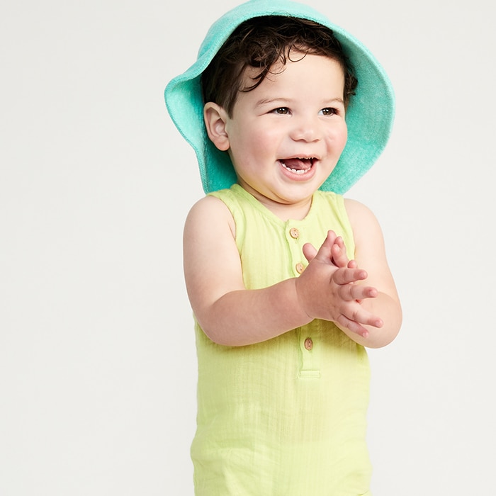 Baby model wearing light green romper with turquoise hat.