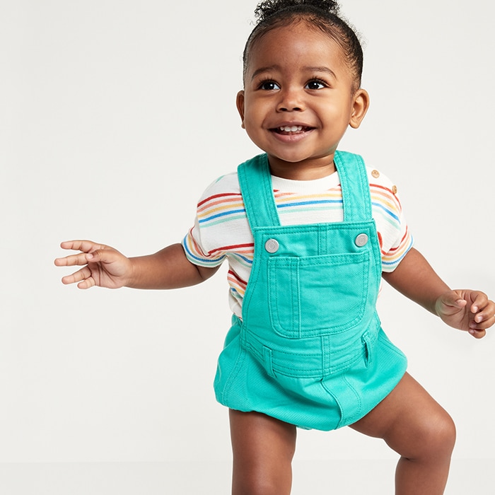 Baby model wearing rainbow striped t-shirt with turquoise overalls.
