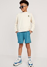 Young model wearing white long-sleeve graphic t-shirt with blue active shorts, striped crew socks and sneakers.